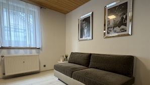 A modern living room with a grey sofa, a radiator, a small side table with a plant, and two framed pictures on the wall.