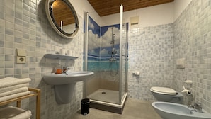A bathroom with a shower, toilet, bidet, sink, and a towel rack.