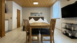 A modern room with a wooden ceiling, a bed with white bedding, a TV mounted on the wall, and a dining table with chairs.