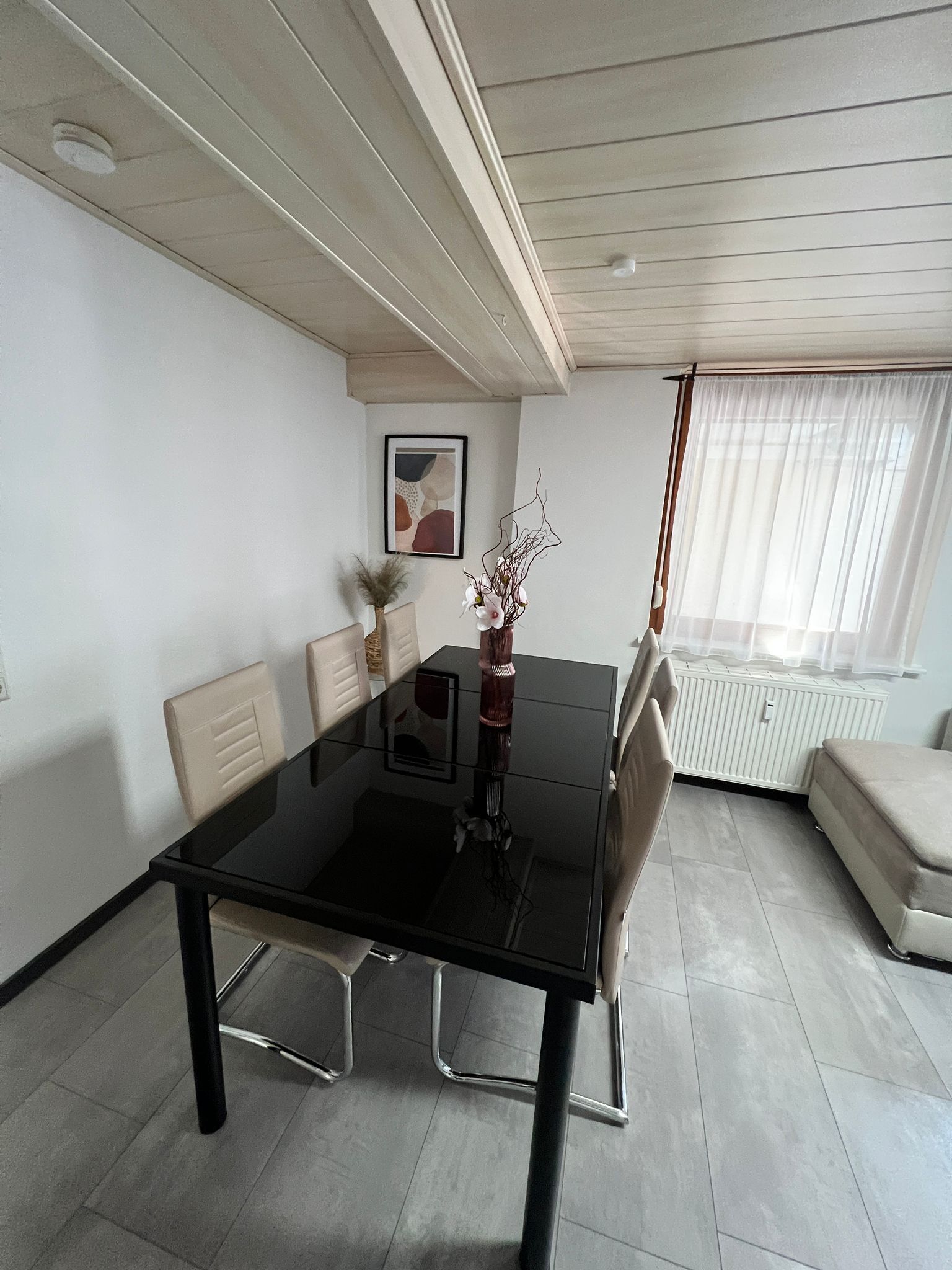 Een moderne eetruimte met een glazen tafel, metalen stoelen en een vaas met bloemen.
