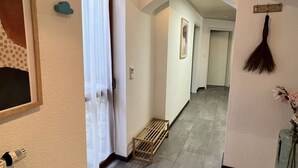 Un pasillo con piso de madera, una puerta con cortina, una escoba en la pared y un pequeño banco de madera.
