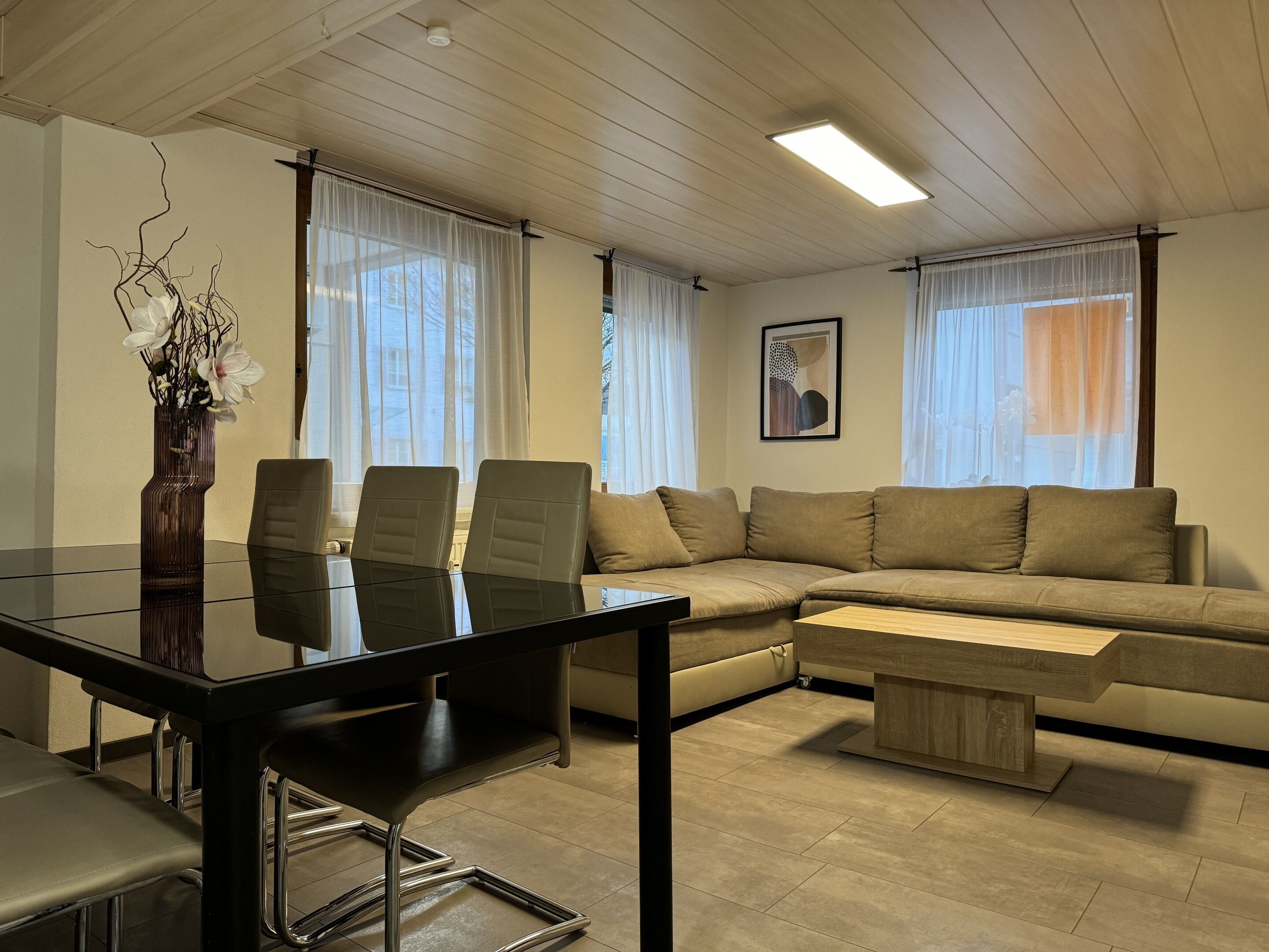 En moderne stue med et glasbord, læderstole, en beige sofa og et træsofabord.