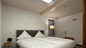 Un dormitorio con una cama grande, una mesita de noche con lámpara e iluminación en el techo.
