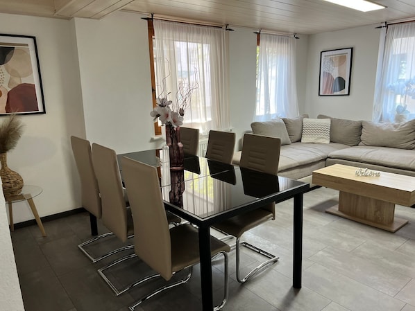 Uma sala de estar moderna com uma mesa de jantar de vidro, sofá bege e um letreiro com a palavra 'Welcome'.