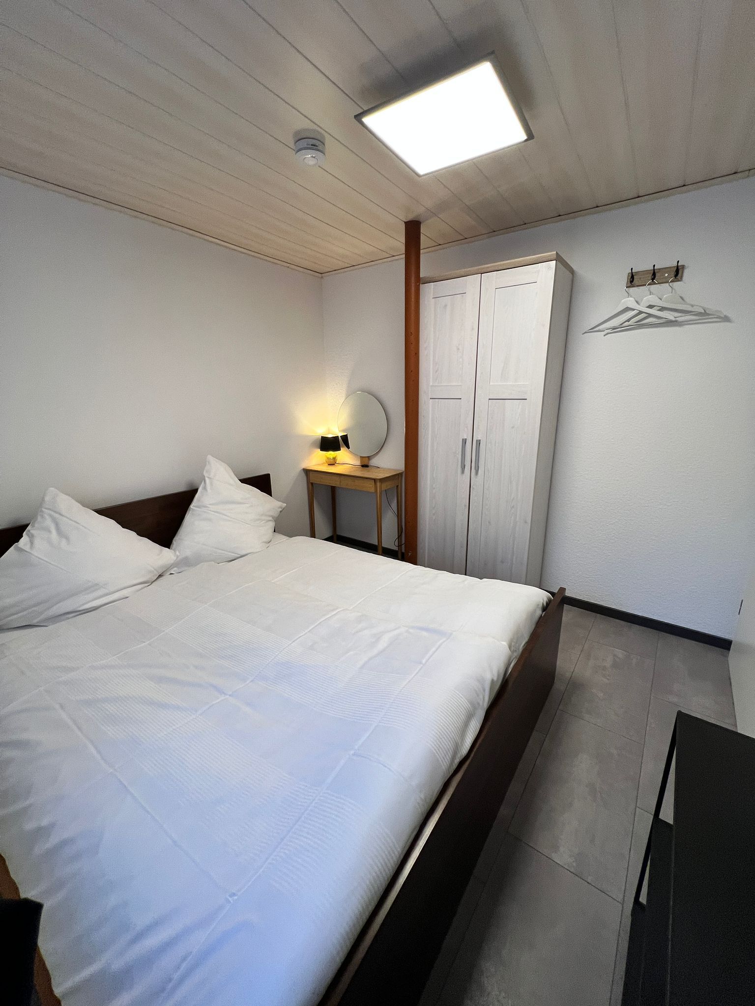A bedroom with a bed, a bedside table with a lamp, a mirror, and a wardrobe.