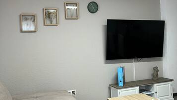 Een woonkamer met een bank, een salontafel, een televisie en lijstjes met foto’s aan de muur.