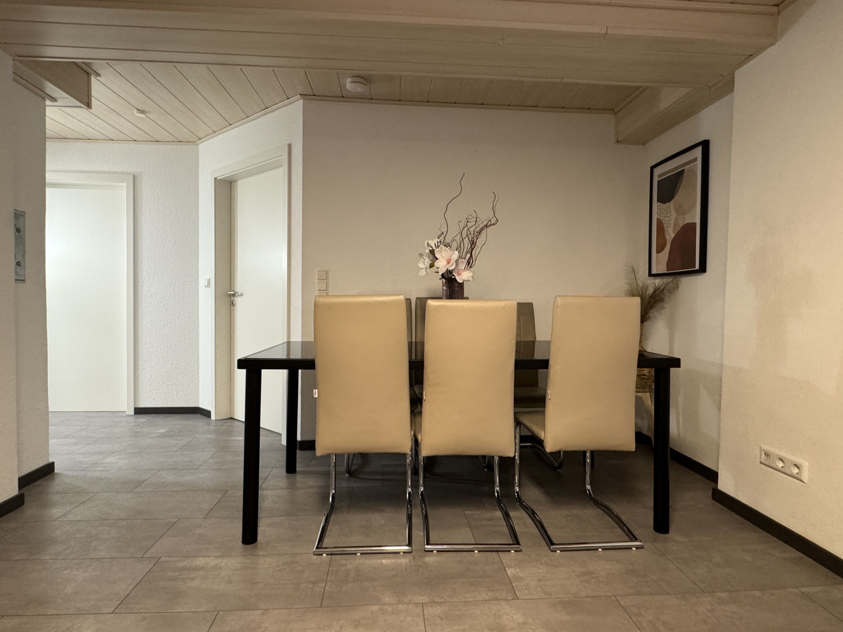 Ein Essbereich mit Tisch und vier Stühlen, einer Vase mit Blumen und einem gerahmten Bild an der Wand.