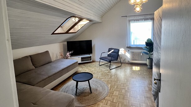 A modern living room with a sloped ceiling, a flat-screen TV, a sofa, a chair, and a small table. - Ferienhaus Möhrle 7 (Ueberlingen)