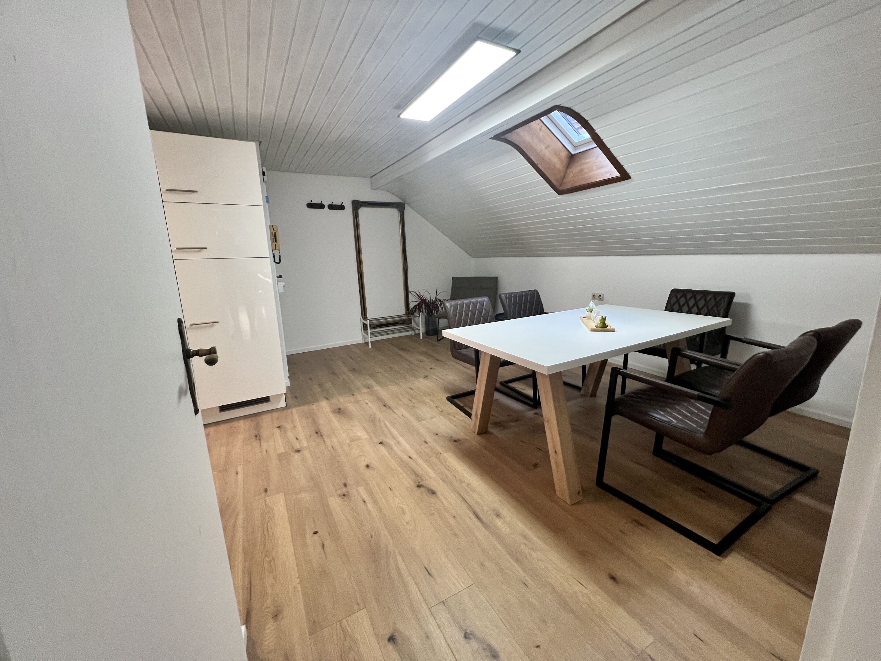 A compact, well-lit room with a dining table, chairs, and a kitchenette.
