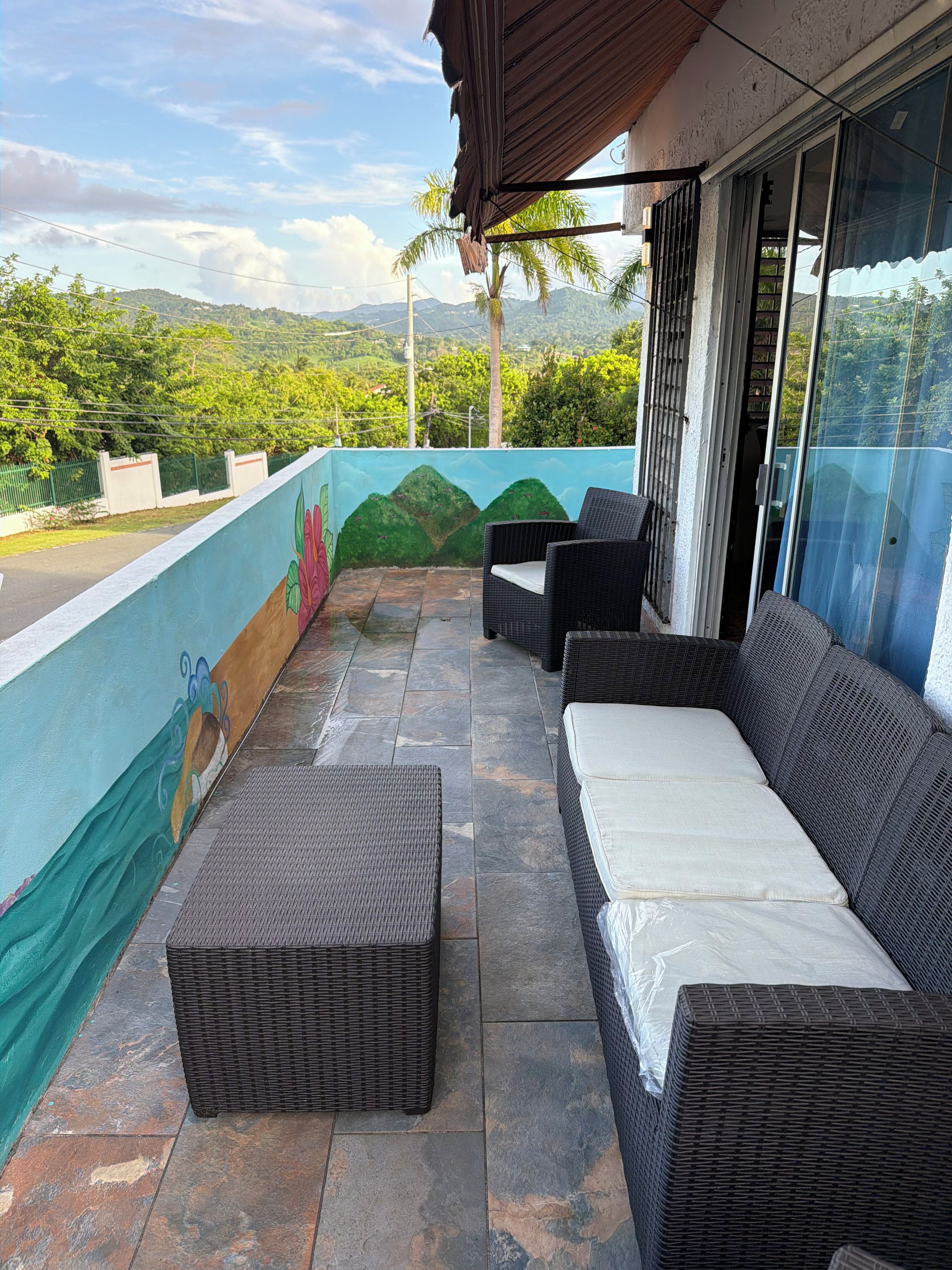 A balcony with wicker furniture, a view of green hills, and a mural on the wall.