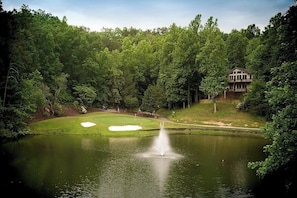 Un campo de golf con un estanque, una fuente y un edificio al fondo.