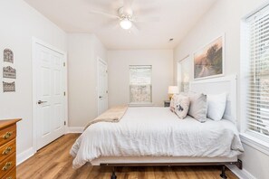 A bedroom with a bed, a ceiling fan, a window with blinds, and a door.