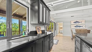 A modern kitchen with black cabinets, a large island with a sink, and a view of the outdoors.