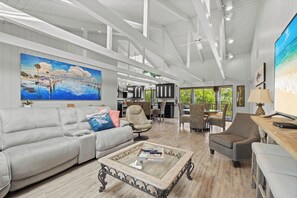 A spacious living area with a large painting, a sofa, a coffee table, and a dining area with chairs. - Luxury Canal-Front Rental on Longboat Key | Pool, Dock & Lift (Longboat Key)