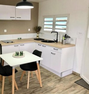 Uma cozinha compacta com armários brancos, micro-ondas e pia. Há uma mesa de jantar com duas cadeiras.