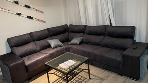 Ein modernes Wohnzimmer mit einem dunkelbraunen Ecksofa, einem Glastisch und einer Wanddekoration zum Thema Skifahren.