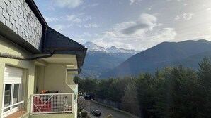 Ein Wohngebäude mit Balkon und Blick auf schneebedeckte Berge, sowie eine Straße mit parkenden Autos.