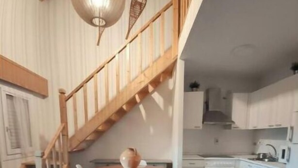 Eine moderne Küche mit weißen Schränken, einer Holztreppe und einem Essbereich mit rundem Tisch und Stühlen.