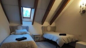 Ein kleines Schlafzimmer im Dachgeschoss mit zwei Betten, Holzbalkendecke und einem Oberlicht.