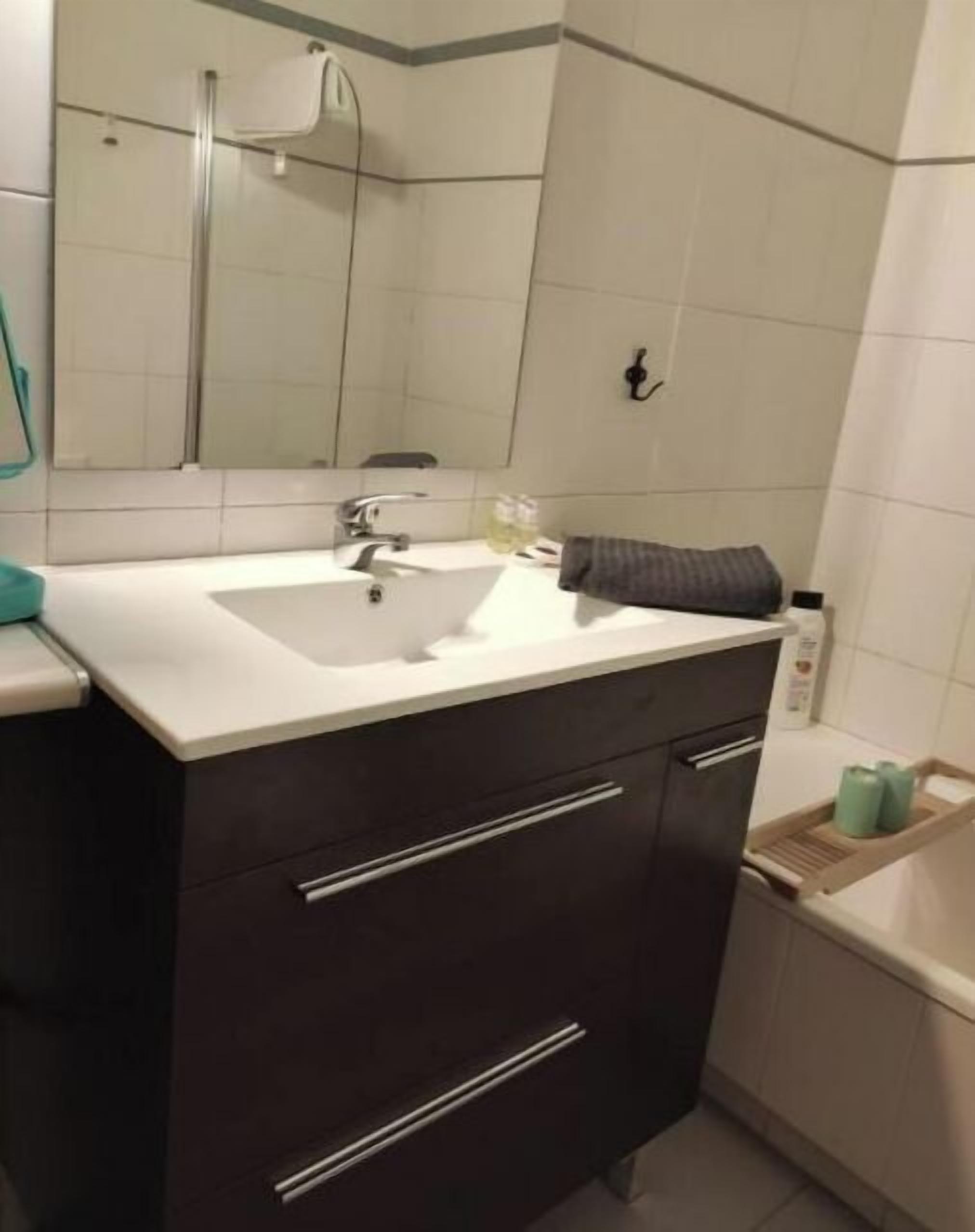 Une salle de bain moderne avec un lavabo blanc, des meubles de rangement aux couleurs sombres et un miroir au-dessus.