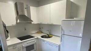 Eine kompakte Küche mit weißen Schränken, einer Edelstahl-Dunstabzugshaube, einem Spülbecken, einem Geschirrspüler und einem Kühlschrank.