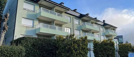 A multi-story residential building with balconies, a paved driveway, and a well-maintained hedge.