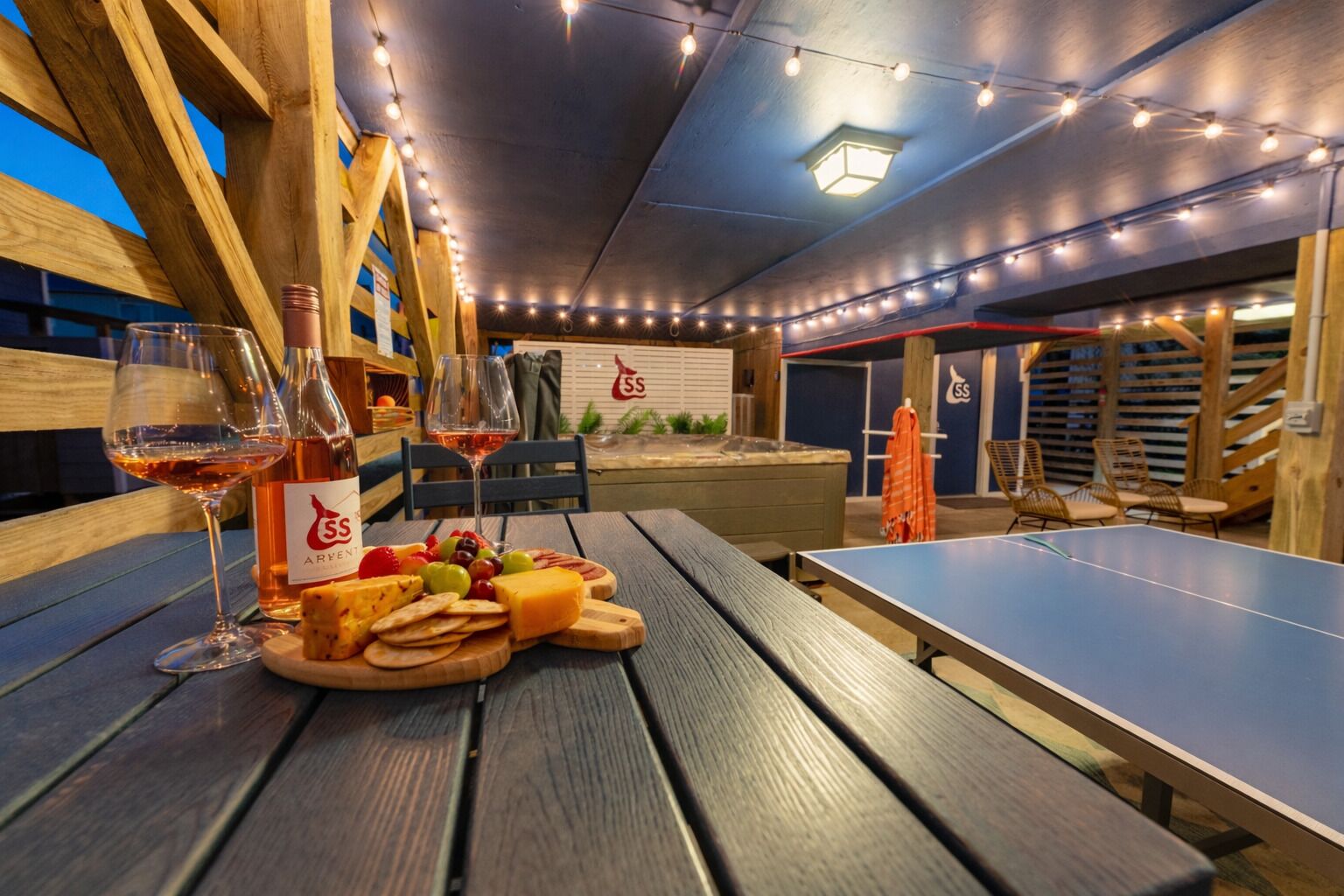 Area esterna con posti a sedere, un tavolo da ping pong, panche di legno e un tavolo con cibo e bevande.