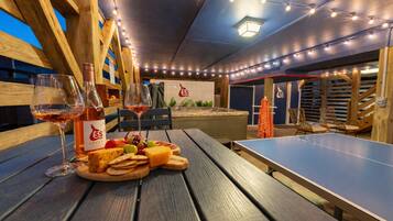 Area esterna con posti a sedere, un tavolo da ping pong, panche di legno e un tavolo con cibo e bevande.