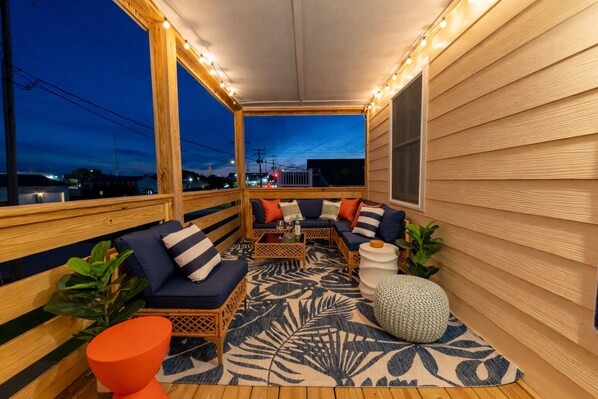 A covered outdoor seating area with a sofa set, a small table, and a patterned rug.