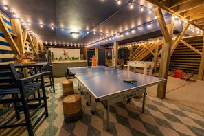 A ping pong table in a room with a checkered floor, wooden beams, and string lights.