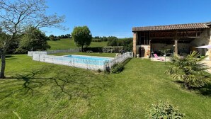 Una piscina con cerca blanca, césped y un edificio con tejado de baldosas.