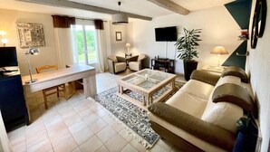 Amplia sala de estar con sofá, mesa de centro y televisor. Hay una zona de comedor con mesa y sillas, y un amplio ventanal que proporciona luz natural.