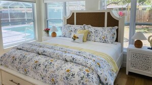 A bedroom with a large bed, a wooden headboard, and a view of a swimming pool through large windows. - Private Pool and Close to Clearwater beach! Perfect for any family! (Clearwater)