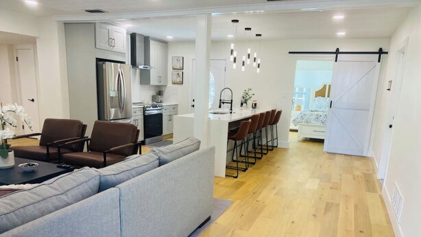 A modern kitchen with a built-in oven, a refrigerator, and a dining area with a grey sofa and brown chairs. - Private Pool and Close to Clearwater beach! Perfect for any family! (Clearwater)