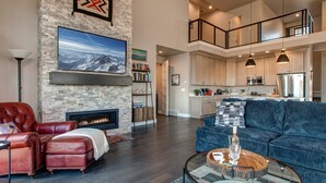 A spacious living area with a fireplace, leather furniture, and a modern kitchen in the background. - Near Jordanelle & Deer Valley with Mountain & Lake Views, Hot Tub, Game Room & More! (Heber City)