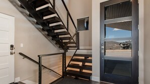 A modern interior with a staircase, a door with a window, and a view of a house outside. - Near Jordanelle & Deer Valley with Mountain & Lake Views, Hot Tub, Game Room & More! (Heber City)
