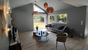 En moderne stue med stort vindue, sofa, sofabord og hængende pendellamper.