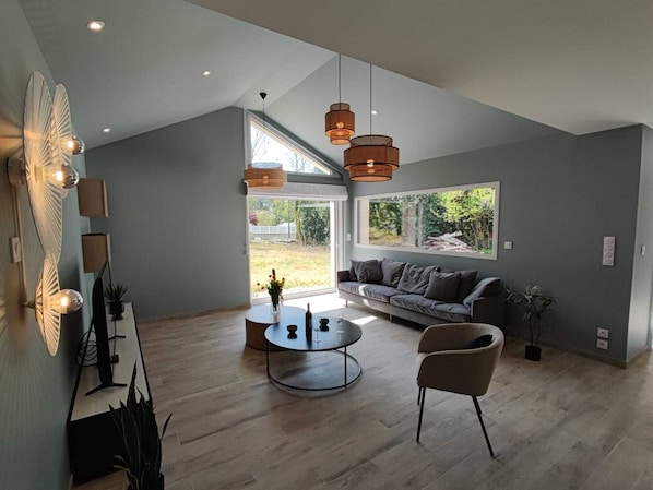 A modern living room with a large window, a sofa, a coffee table, and hanging pendant lights.