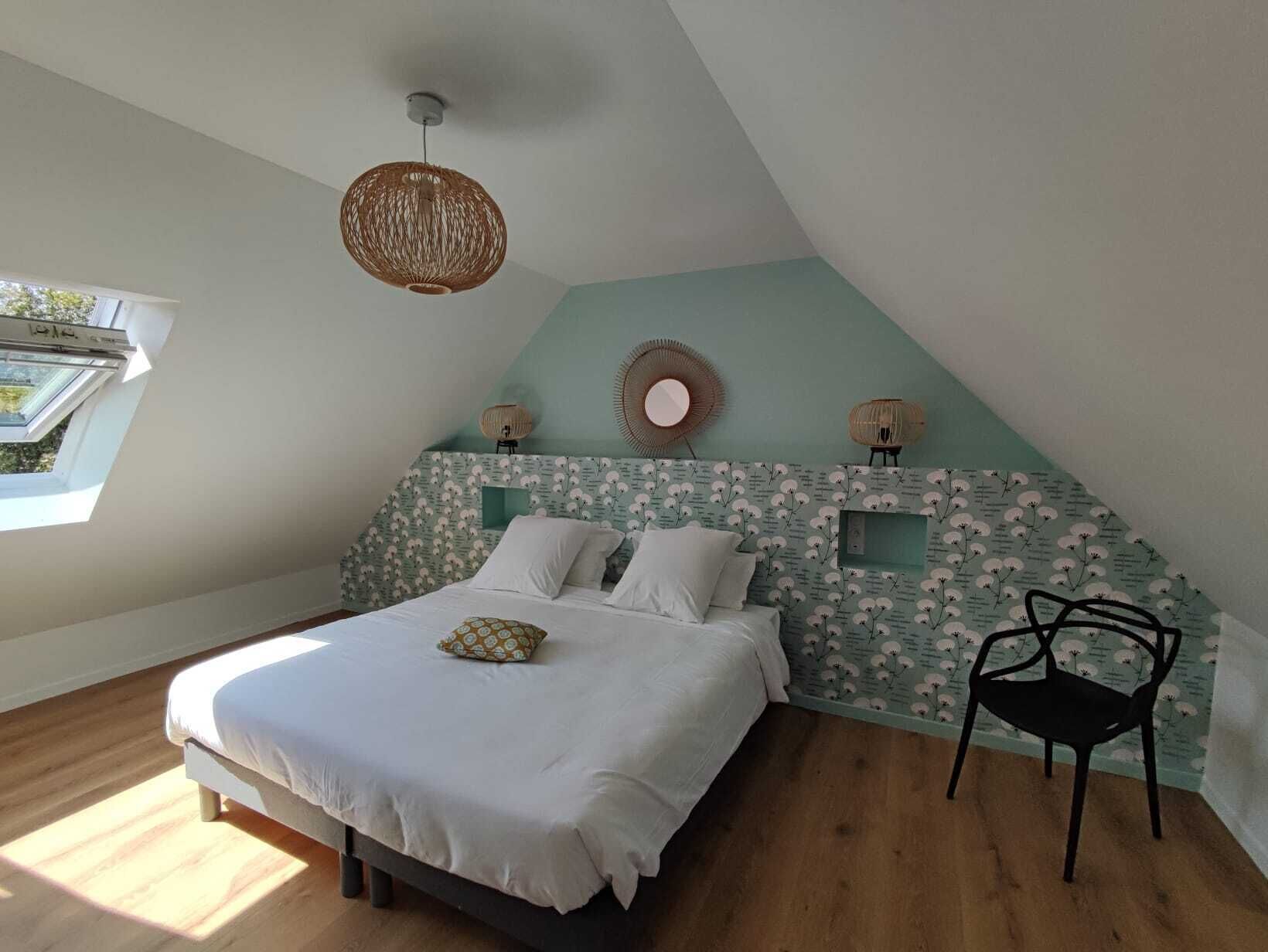 A bedroom with a sloped ceiling, a bed with white bedding, a woven light fixture, and a small chair.
