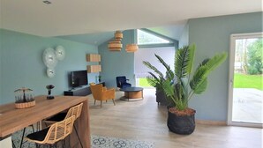En moderne stue med et træspisebord, fletstole, en sofa og en stor potteplante.