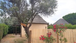 Un espace extérieur rustique agrémenté d’une clôture en bois, d’un arbre et d’une structure au toit de chaume.