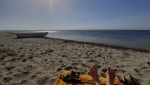 Une plage avec un bateau et une personne allongée sur une couverture.