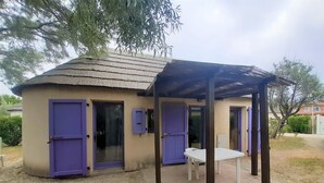 Un petit bâtiment doté d’un patio couvert, comprenant une table et des chaises, ainsi que deux portes avec des volets violets.