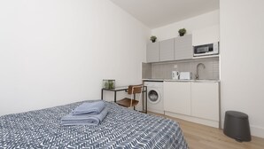 Una habitación moderna y compacta con una cama bien hecha, una lavadora y una pequeña kitchenette.
