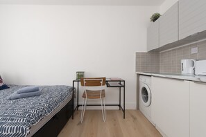 Une pièce de taille modeste comprenant un lit, un bureau, une chaise, un lave-linge et un petit coin cuisine.