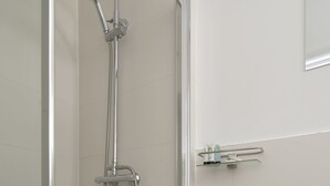 Ducha con puerta de vidrio, lavabo con espejo y una pequeña estantería con artículos de aseo.