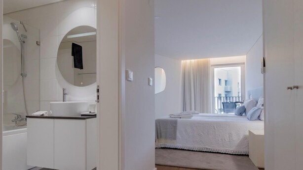 A modern hotel room with a bathroom, a bed with a view, and a small balcony.