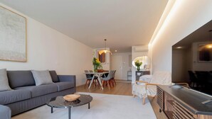 A modern living room with a grey sofa, a coffee table, and a dining area with chairs and a table.