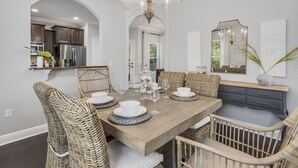 A dining area with a wooden table set for four, surrounded by wicker chairs. A chandelier hangs above, and a mirror is on the wall. - Walk to the Beach ~ Biking Trails (Santa Rosa Beach)