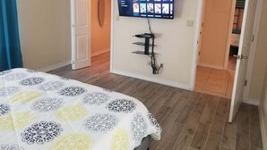 A bedroom with a bed, a TV mounted on the wall, and a door leading to another room. - Oversized 2 Bedroom - Modern - Pool Near Beach (South Padre Island)